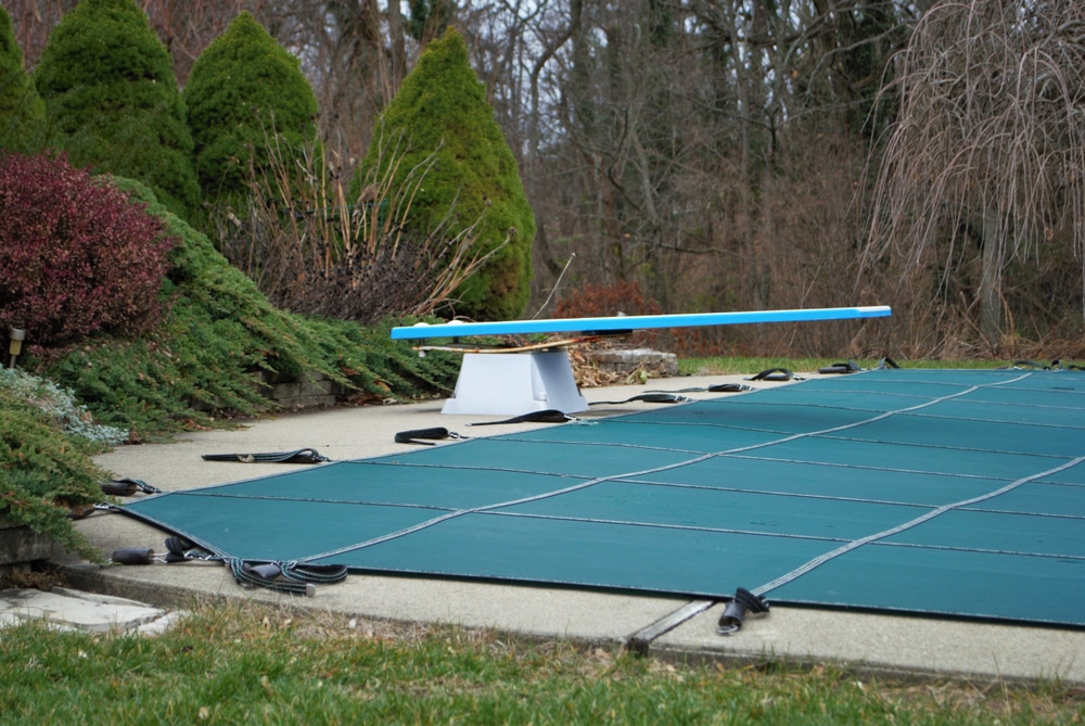 backyard swimming pool with diving board and pool slide tarped up and closed down for winter