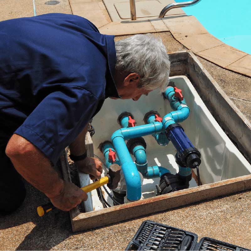 A Technician Repairing Pool Plumbing And Equipment Near A Swimming Pool