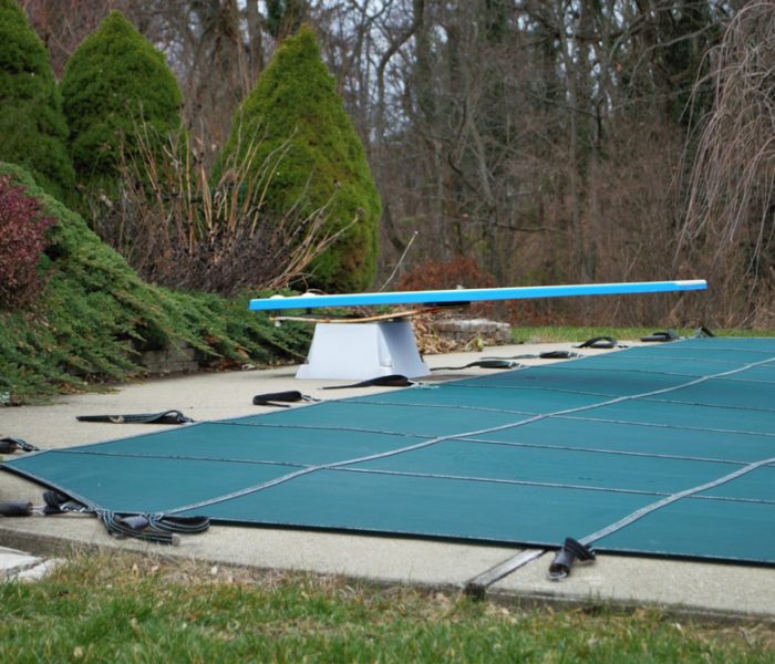 backyard swimming pool with diving board and pool slide tarped up and closed down for winter